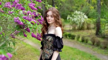 Çiçekli leylak bahçesinde poz veren klasik korse giymiş romantik bir kadının videosu.
