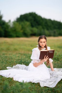Klasik beyaz dantelli genç kadınlar doğada huzurlu bir pikniğin tadını çıkarıyorlar. Yumuşak doğal ışık, romantik atmosfer, eski tarz.