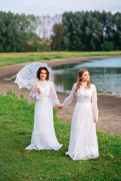 Klasik beyaz dantelli genç kadınlar doğada huzurlu bir pikniğin tadını çıkarıyorlar. Yumuşak doğal ışık, romantik atmosfer, eski tarz.