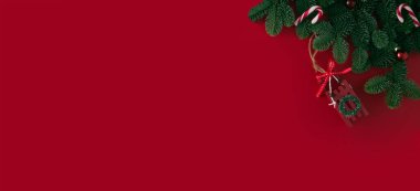 Kırmızı arka plan üzerinde şenlik dekoru olan bir Noel ağacının yeşil dalları.