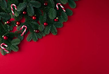 Kırmızı arka plan üzerinde şenlik dekoru olan bir Noel ağacının yeşil dalları.