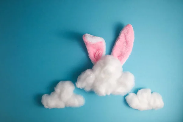 Bunny ears peeking out from behind white clouds of cotton wool on a blue background copy space