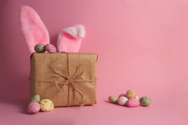Gift box with cute bunny ears and easter eggs on pink background copy space. High quality photo