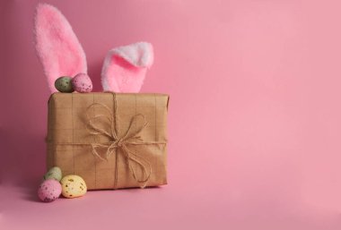 Gift box with cute bunny ears and easter eggs on pink background copy space. High quality photo