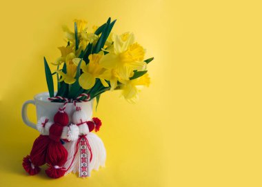 Bouquet of yellow daffodils tied with red-white martenitsa, martisor on yellow background copy space