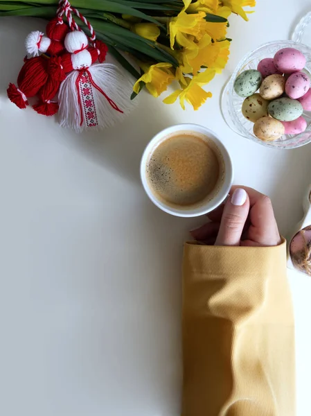 Bouquet of daffodils with red and white martenitsa and a womans hand holding a cup of coffee