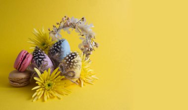 Easter eggs in a composition with yellow flowers and macaroons on a yellow background copy space