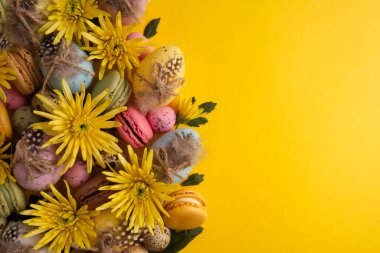 Easter eggs in a composition with yellow flowers and macaroons on a yellow background copy space
