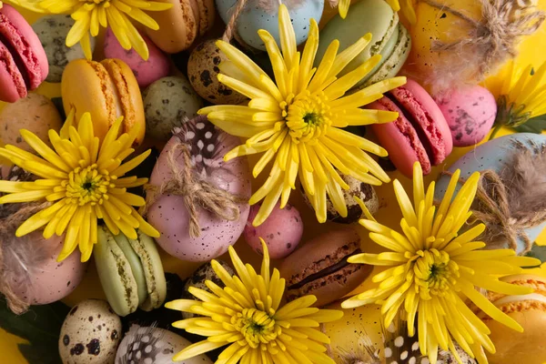 Easter eggs in a composition with yellow flowers and macaroons on a yellow background copy space