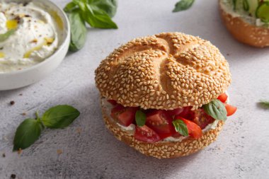 Bun with sesame seeds with cheese cream and fresh tomatoes with basil leaves close up