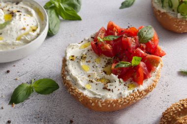 Bun with sesame seeds with cheese cream and fresh tomatoes with basil leaves close up