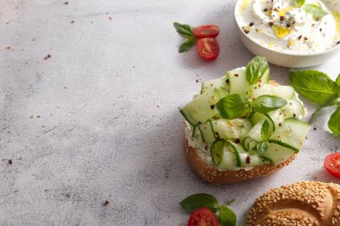 Bun with sesame seeds with cheese cream and fresh cucumbers with basil leaves copy space