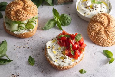 Bun with sesame seeds with cheese cream and fresh tomatoes with basil leaves close up