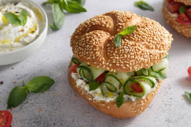 Bun with sesame seeds with cheese cream and fresh cucumbers with basil leaves close-up
