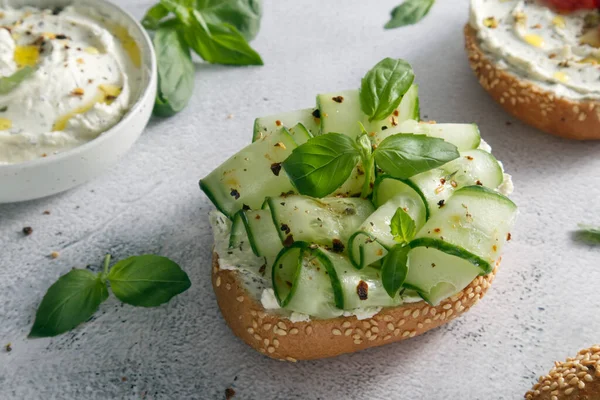 Bun with sesame seeds with cheese cream and fresh cucumbers with basil leaves close-up