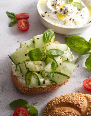 Bun with sesame seeds with cheese cream and fresh cucumbers with basil leaves close-up