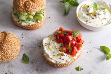 Bun with sesame seeds with cheese cream and fresh tomatoes with basil leaves close up