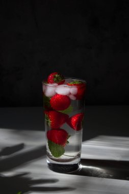 Refreshing drink with strawberries, mint and ice in hard sunlight with interesting shadows close up