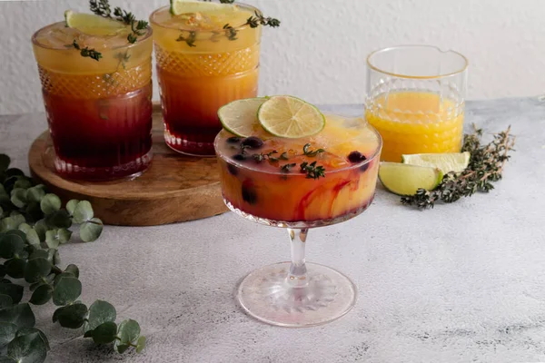 Cocktails with ice, orange juice and grenadine syrup decorated with berries and herbs close-up