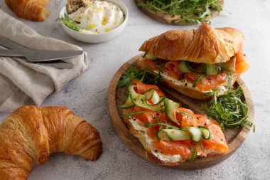Croissants with cheese cream, red fish and cucumber on a wooden stand for breakfast or lunch closeup