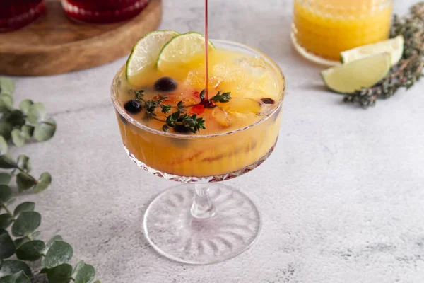 Cocktail with ice, orange juice and grenadine syrup decorated with berries and herbs close-up