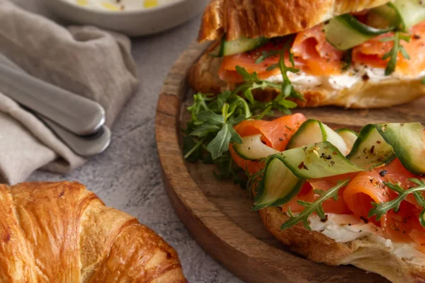 Croissants with cheese cream, red fish and cucumber on a wooden stand for breakfast or lunch closeup