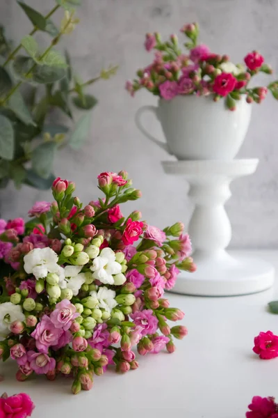 Bouquet of flowers on the table against the background of a cup of flowers on a white stand close up