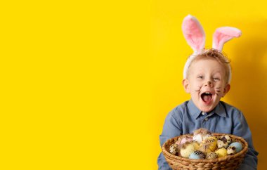 Boy with bunny ears holding basket with easter eggs on yellow background copy space. High quality 