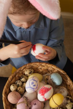 Cute boy with bunny ears paints Easter eggs close up. High quality photo