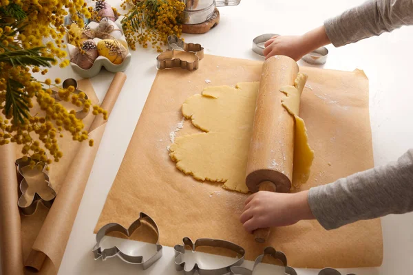 Çocuklar Paskalya kurabiyeleri için hamuru bahar dekorunda masanın üstüne sererler.