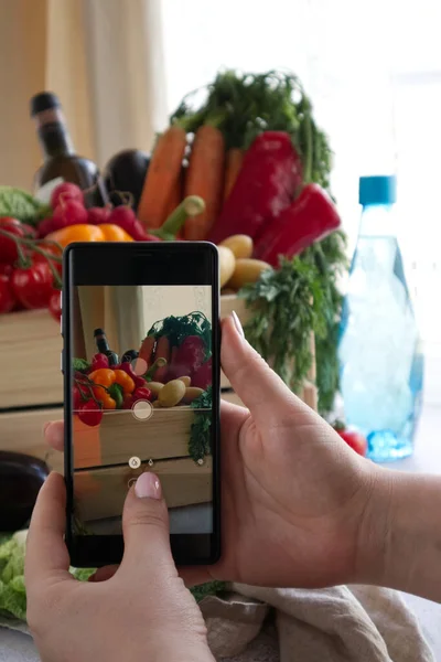 Eller akıllı telefondan fotoğraf çeker. Teslimat için hazırlanmış taze ürünlerle dolu bir kutu.