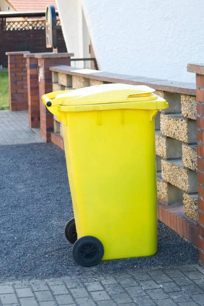 Yellow garbage container near the stone fence close-up. High quality photo