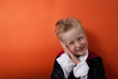 Vampir kostümlü bir çocuk duygusal olarak turuncu arka plandaki kameraya bakıyor. Kaliteli fotoğraf