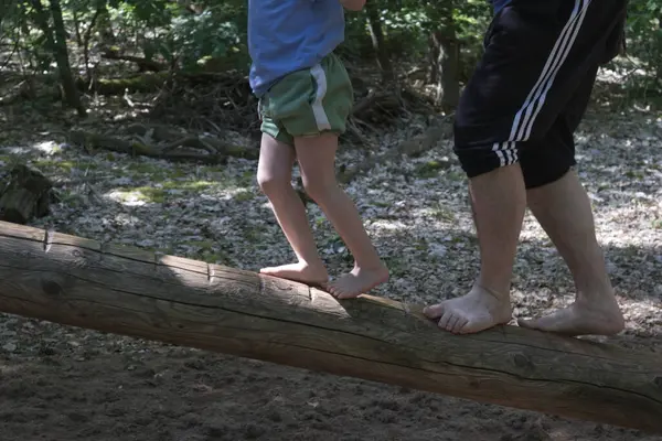Barefoot man and child balancing on a wooden log close-up