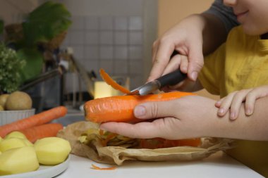 Bir çocuğa mutfakta havuç nasıl soyulacağını dikkatlice gösteren kadın ellerine yakın plan. Yüksek kalite