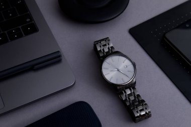 Bir dizüstü bilgisayar, şarj aleti, telefon ve şık kol saati tasarımı. 