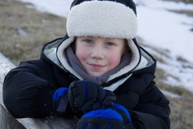 Kışın giyinmiş bir çocuğun portresini karla kaplı bir çayırın arka planına yakın tut.