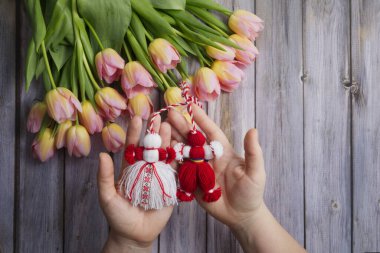 Martenitsa, Martisor kadın ellerinde. Ahşap masa manzaralı pembe lalelerin arka planına karşı.