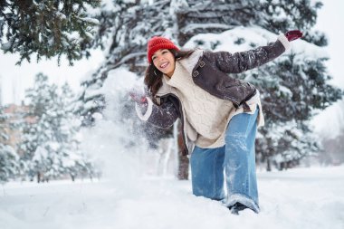 Güzel bir kadın karlı ağaçların arasında duruyor ve ilk karın tadını çıkarıyor. Tatiller, dinlenme, seyahat konsepti.