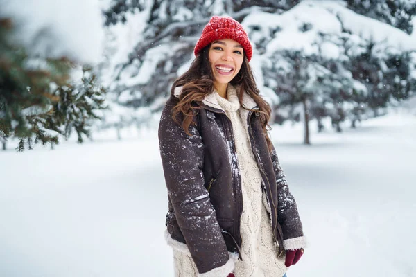 Beautiful woman standing among snowy trees and enjoying first snow. Holidays, rest, travel concept.