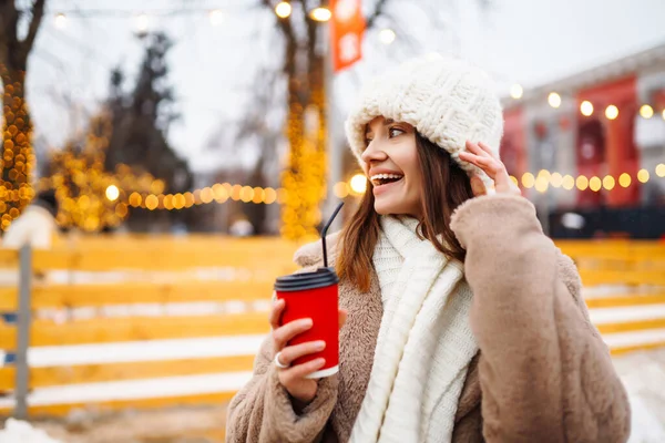 stock image Beautiful woman  drinking hot coffee while walking in the  city market decorated with holiday lights. Holidays, rest, travel concept.