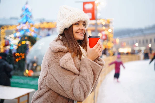 stock image Beautiful woman  drinking hot coffee while walking in the  city market decorated with holiday lights. Holidays, rest, travel concept.