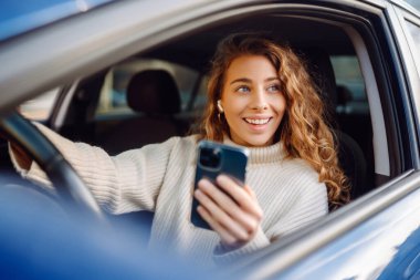 Araba sürerken akıllı telefonuyla mesaj atan genç bir kadının portresi. Araba paylaşımı, kiralama servisi veya taksi uygulaması.