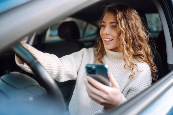 一个年轻女子开车时用智能手机发短信的肖像 汽车共享 租赁服务或出租车应用程序 — 图库照片