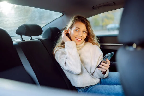 漂亮的女人坐在车后座上 一边用智能手机一边笑 Business Technology Blog Concept — 图库照片