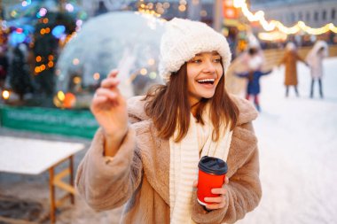 Arka planda buz pateni pistinde tek kullanımlık kahve fincanı olan mutlu bir kadın. Noel, sıcak içecekler ve tatil konsepti.