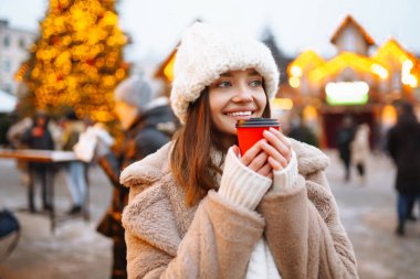 Arka planda buz pateni pistinde tek kullanımlık kahve fincanı olan mutlu bir kadın. Noel, sıcak içecekler ve tatil konsepti.