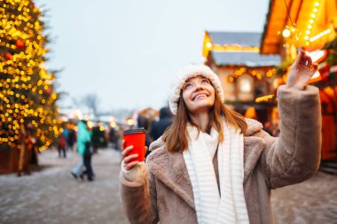 Arka planda buz pateni pistinde tek kullanımlık kahve fincanı olan mutlu bir kadın. Noel, sıcak içecekler ve tatil konsepti.