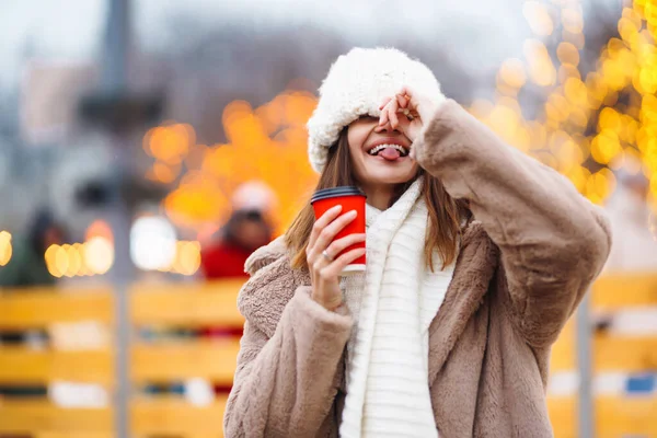 stock image Happy woman with disposable paper coffee cup in winter over outdoor ice skating rink on background. Christmas, hot drinks and holidays concept.