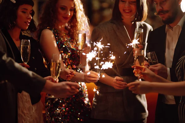 Sparkling sparklers in the hands of friends. Young people having fun with fire sparklers at night time. Holidays, vacation, relax, party and lifestyle concept.